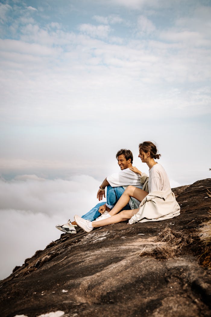 team-06 A couple sits on a mountain edge, enjoying a serene view above clouds.