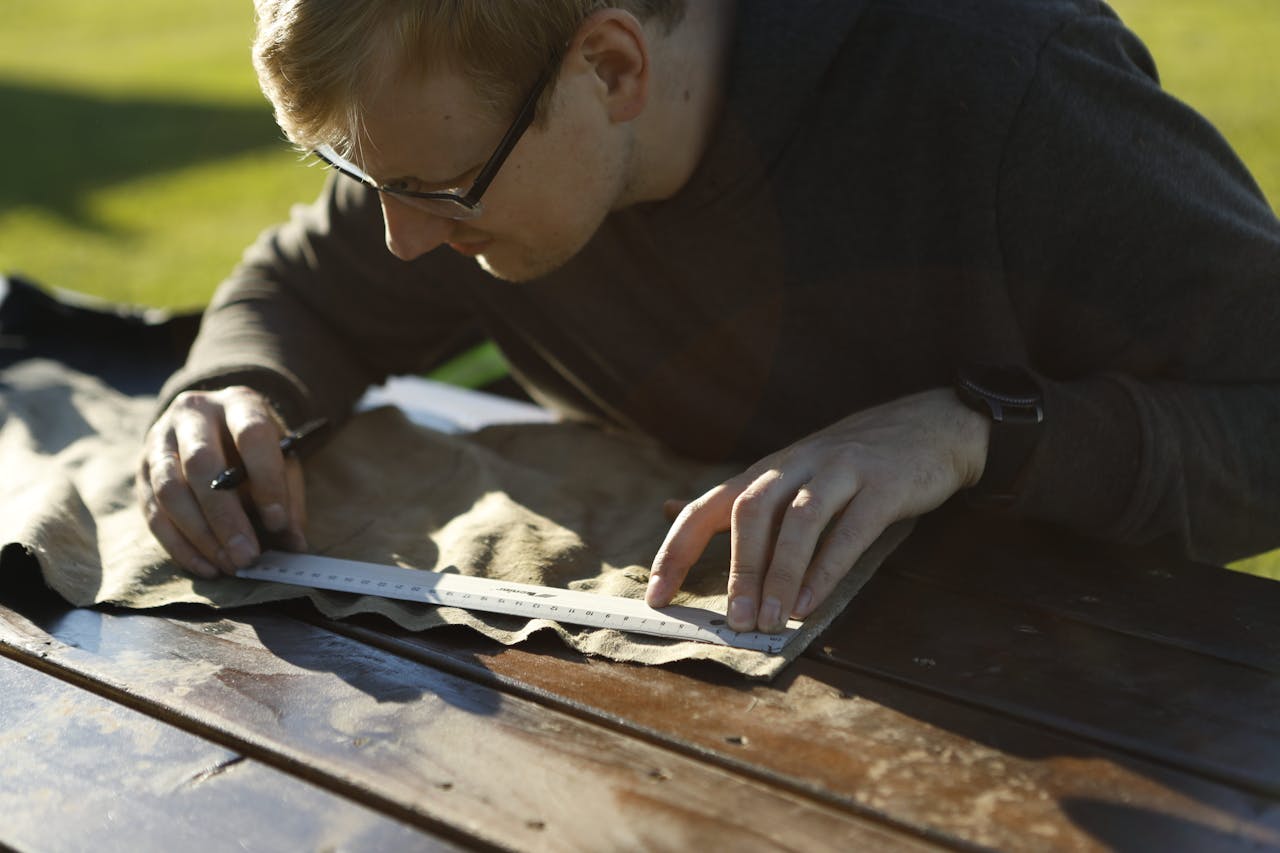 embark A focused man measuring fabric with a ruler outdoors in Estonia, highlighting precision in craftwork.