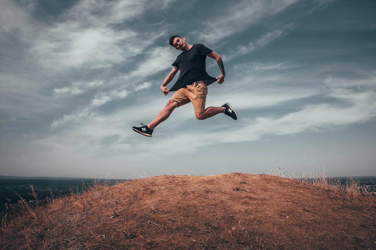 services-03 Young man jumping on a hilltop under a dramatic sky, capturing energy and freedom outdoors.