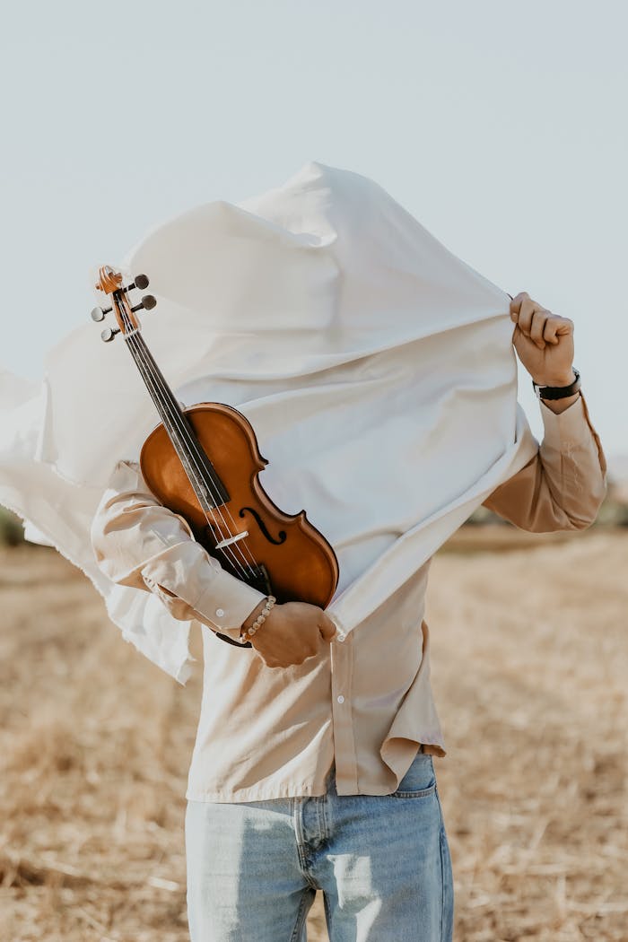 services-04 A person in a rural setting concealing their face with a sheet while holding a violin.