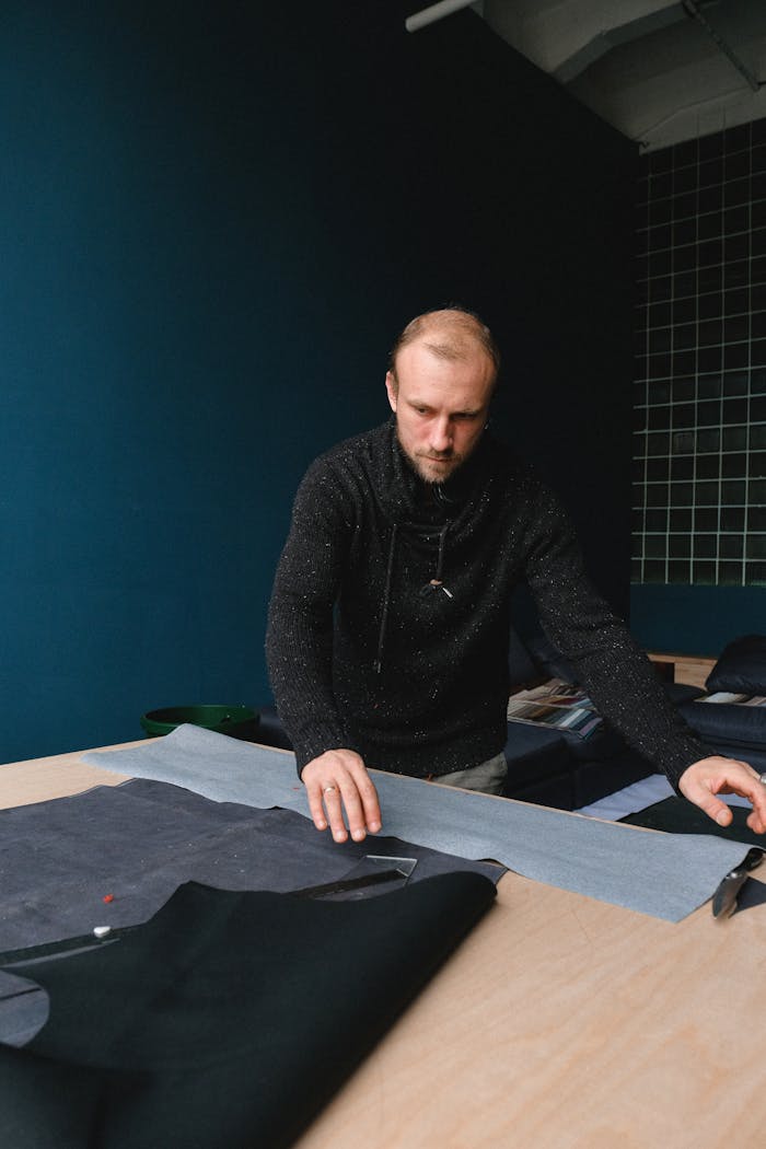 team-01 Focused tailor working on fabric design at workshop table.
