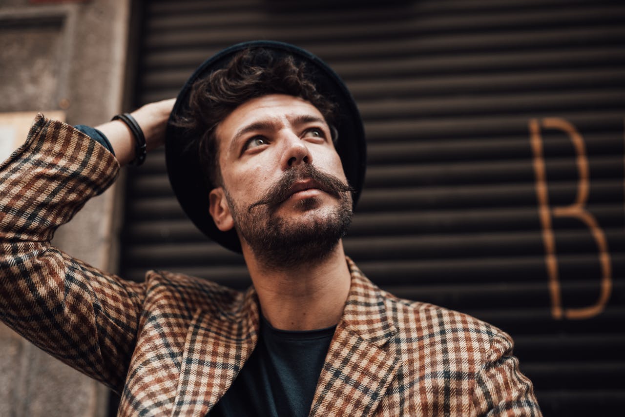 team-02 From below of thoughtful bearded male in trendy outfit touching hat while looking away